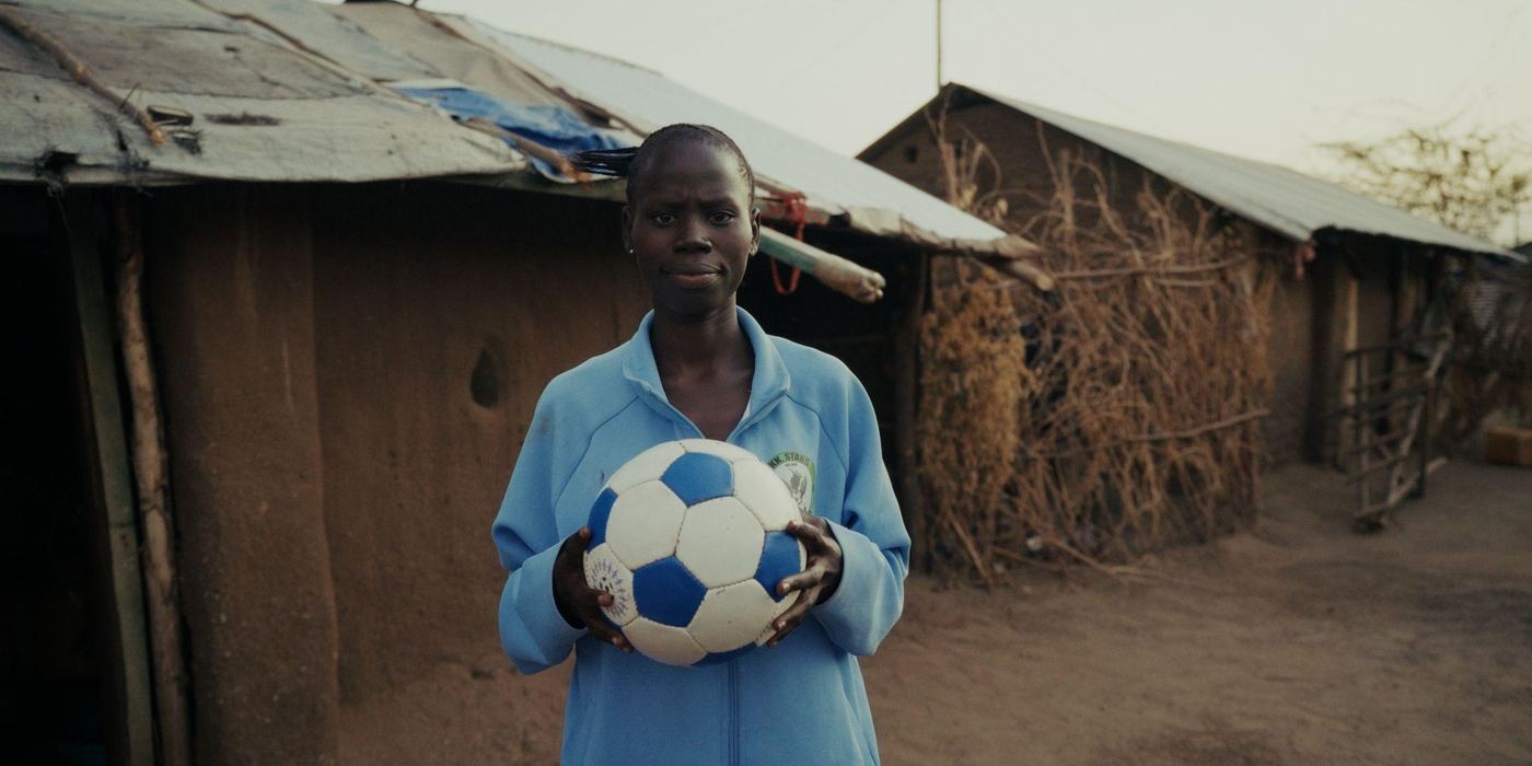A man holds a football between mud-walled homes